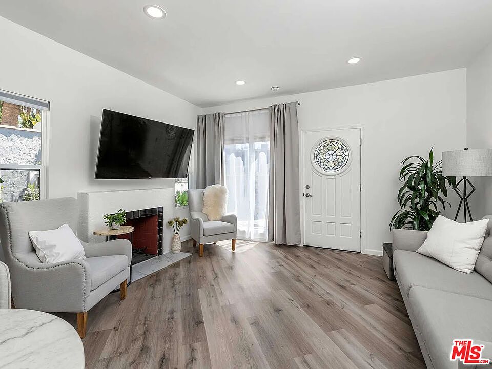 Living room of 8823 Betty Way with a gas fireplace, a stained-glass front door, and light through full-length curtains