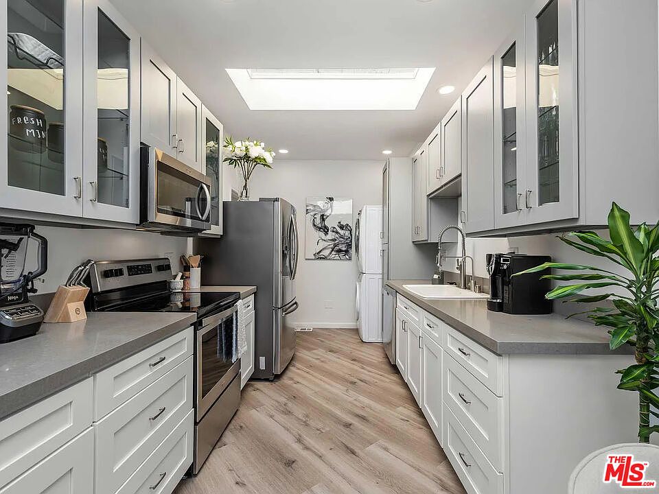Skylit galley kitchen with new stainless appliances, a Samsung smart refrigerator, gray quartz counters, and ample white cabinetry