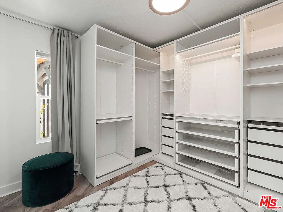 Fully fitted walk-in closet with built-in shelving, drawers, and a hanging system, lit by a corner window