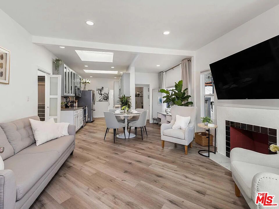 The open living and dining great room of 8823 Betty Way, with a skylit kitchen beyond, pale oak floors, and light pouring through large windows